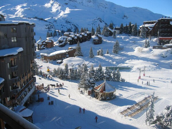 Estación de esquí nevada con edificios de madera, pistas de esquí y montañas al fondo.