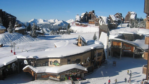 Estación de esquí nevada con edificios de madera, servicios de alquiler de esquíes y un telón de fondo montañoso.