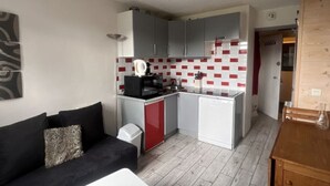 Un espacio habitable compacto con kitchenette, un sofá, una pequeña mesa y un armario de madera.