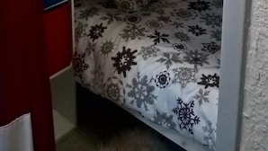 Una cama litera con un colchón estampado de flores, un estante con un cuadro enmarcado y una lámpara fijada a la pared.