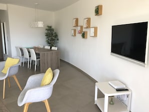 Ein modernes Wohnzimmer mit Essbereich, einem großen Flachbildfernseher an der Wand und einem kleinen weißen Beistelltisch mit einem Laptop.