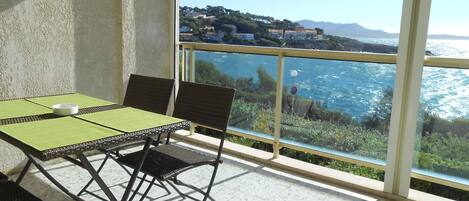 Un balcone con tavolo e sedie, affacciato su una vista costiera con edifici e montagne.
