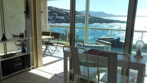 Ein Balkon mit Blick auf das Meer und die Hügel, weiße Stühle, ein kleiner Tisch und ein Regal mit Gegenständen.