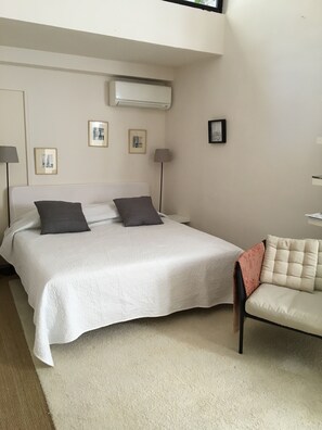 A bedroom with a bed, two bedside lamps, an air conditioner, and framed pictures on the wall.