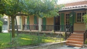 Una casa con porche cubierto, una escalera y un pequeño jardín.
