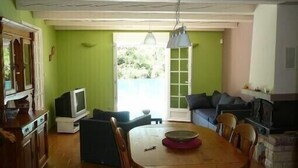 Un comedor con una mesa y sillas de madera, un televisor sobre un mueble bajo y un sofá al fondo.
