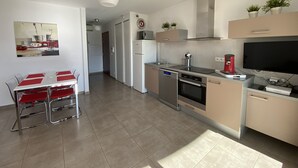 A modern kitchen with stainless steel appliances, a dining area with red chairs, and a flat-screen TV mounted above the counter. - CALVI, 1-bedroom apartment in a residence with ocean views, Wi-Fi, 5 minutes from the beach and downtown, air-conditioned, sleeps 4 (Calvi)