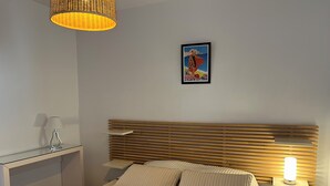A bedroom with a bed, bedside table, lamp, and a poster on the wall. - CALVI, 1-bedroom apartment in a residence with ocean views, Wi-Fi, 5 minutes from the beach and downtown, air-conditioned, sleeps 4 (Calvi)