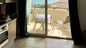 A balcony with a table and chairs, a TV, and a view of the sea. - CALVI, 1-bedroom apartment in a residence with ocean views, Wi-Fi, 5 minutes from the beach and downtown, air-conditioned, sleeps 4 (Calvi)