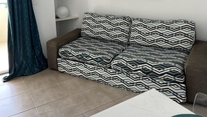 A living room with a sofa, a coffee table, and a wall-mounted abstract painting. - CALVI, 1-bedroom apartment in a residence with ocean views, Wi-Fi, 5 minutes from the beach and downtown, air-conditioned, sleeps 4 (Calvi)