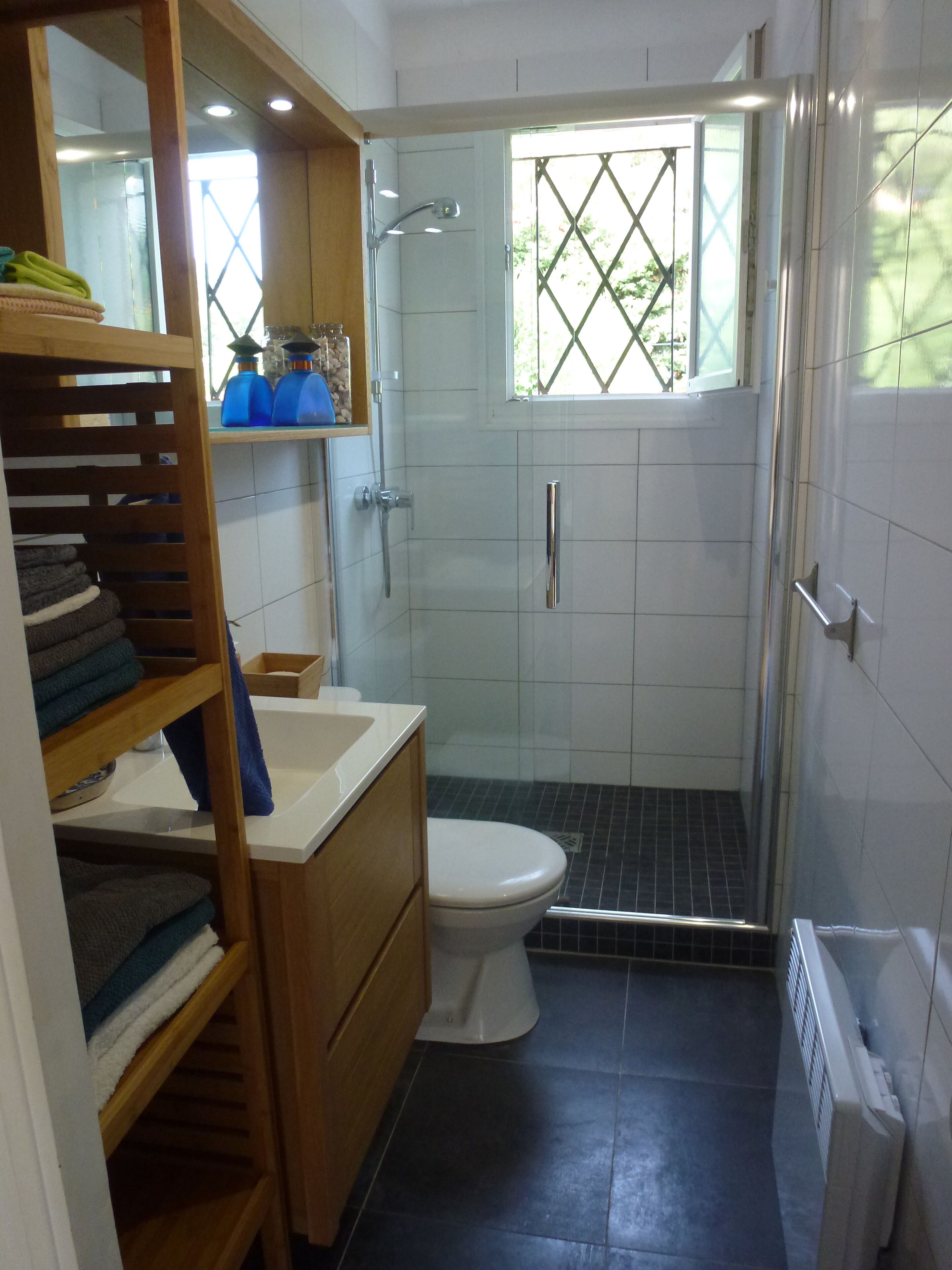 A compact bathroom with a shower, toilet, and built-in shelves with towels.