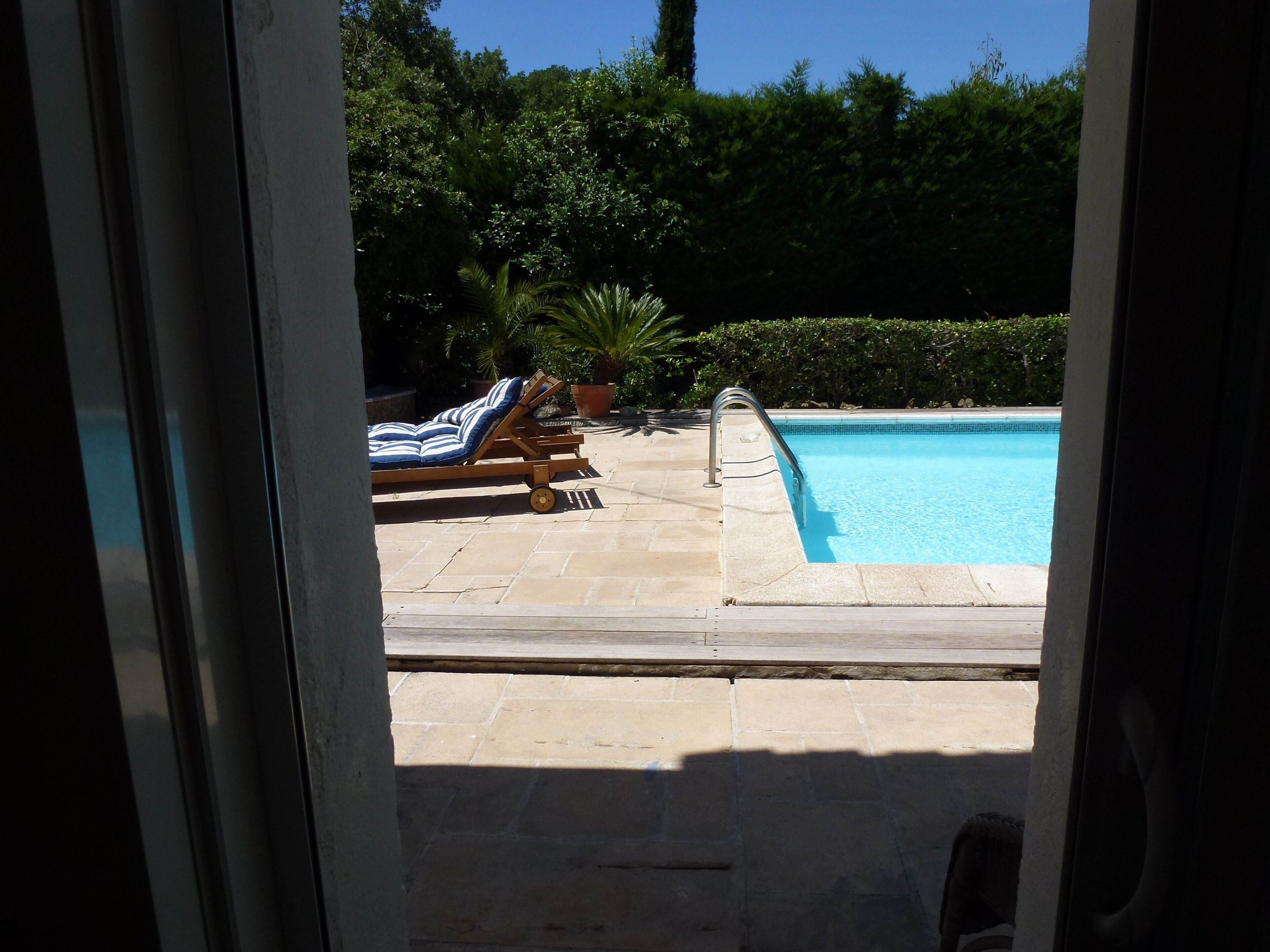 Ein Poolbereich mit Liegestuhl und kleinem Tisch, umgeben von Grün.