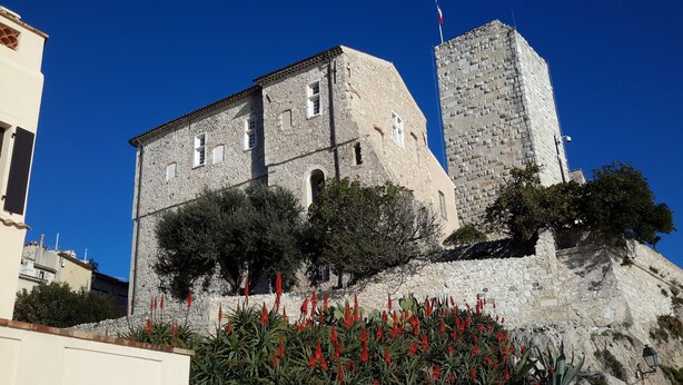 A historic stone building with a prominent tower, surrounded by greenery and red flowers. - Located in old Antibes, 2 steps from shops, sleeps 2 to 3 (Antibes)