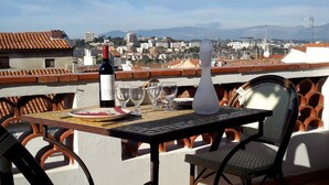 A terrace with a table set for dining, a bottle of wine, and a view of a cityscape with buildings and mountains in the distance. - Located in old Antibes, 2 steps from shops, sleeps 2 to 3 (Antibes)