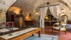Una habitación rústica de paredes de piedra con un banco de madera, una mesa con velas y un sillón con cojín estampado.