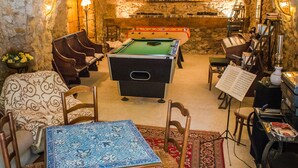 Una habitación acogedora con paredes de piedra, mesa de billar, asientos cómodos y un piano.
