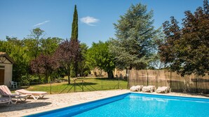 Una piscina con sillas de descanso, un edificio de piedra y un árbol alto en un patio trasero.