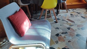 Un coin repas avec un escalier en bois, une table recouverte d’une nappe noire et jaune, et une chaise dotée d’un coussin rouge.