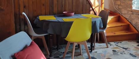 A dining area with a wooden staircase, a table with a black and yellow tablecloth, and a chair with a red cushion.