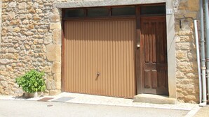 Un bâtiment en pierre avec une grande porte de garage en bois, de nombreuses fenêtres dotées de volets et une petite plante en pot devant.