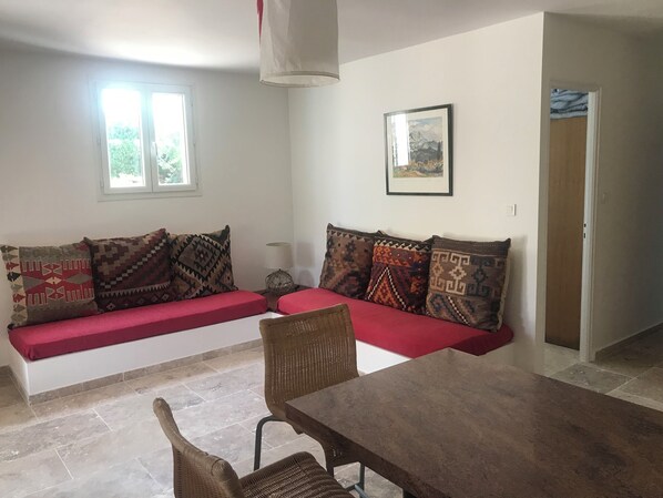Una sala de estar con un sofá, una mesa de comedor y una silla. Hay una ventana y una puerta en la habitación.