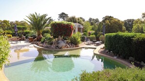 Una piscina circondata da vegetazione rigogliosa, un'area patio con sedie e un piccolo edificio sullo sfondo.