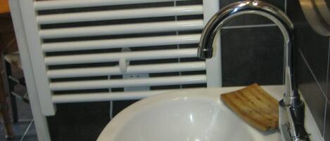 A bathroom with a white sink, a chrome faucet, and a wooden soap dish.