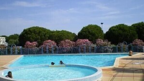 Une piscine dotée d’une terrasse carrelée, entourée d’une clôture et d’arbres.