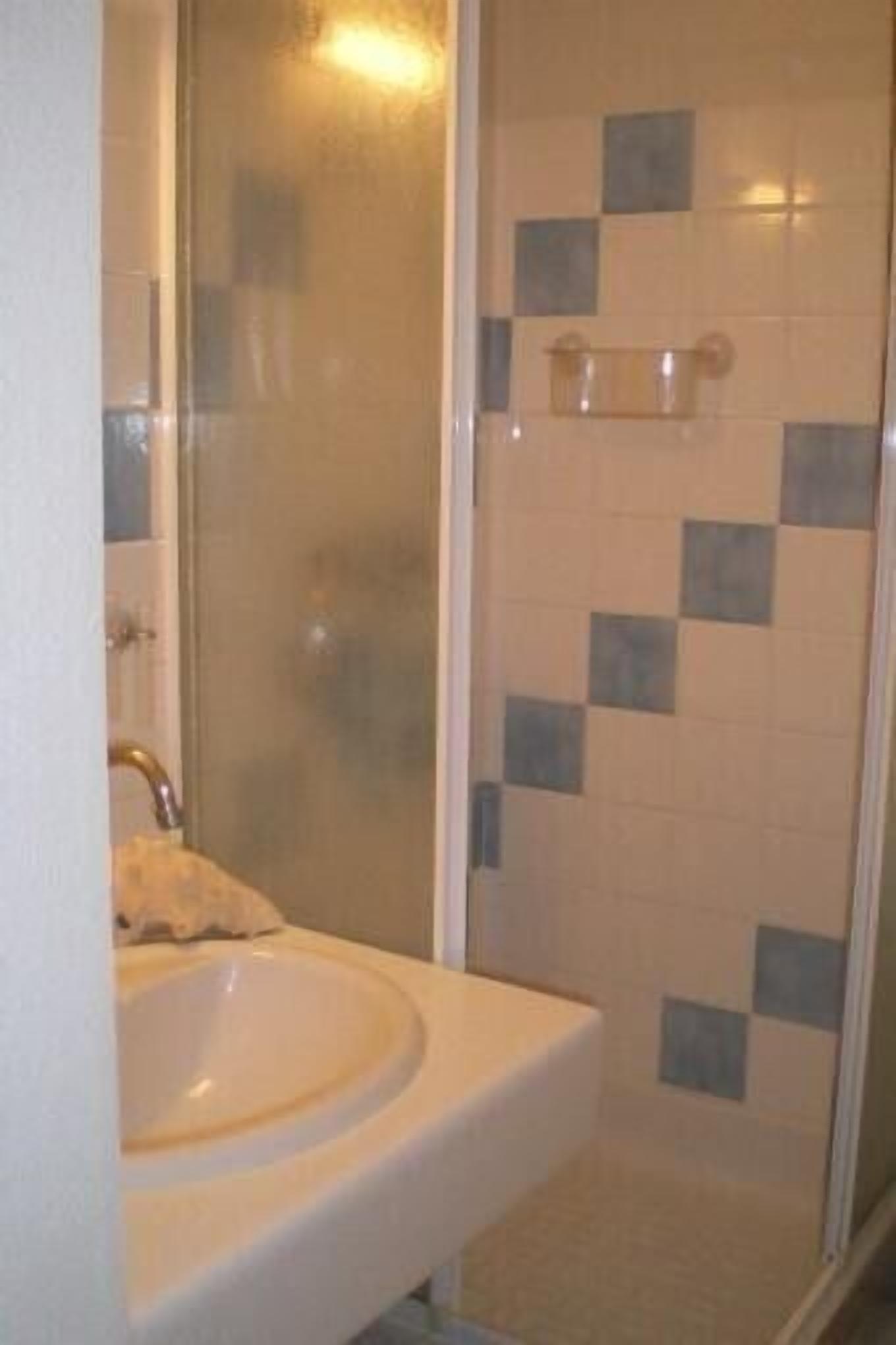 Un baño con ducha de vidrio, un lavamanos blanco y pared de ducha con azulejos.