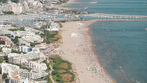 Vue aérienne d’une ville côtière avec une plage, des bâtiments et un port de plaisance.