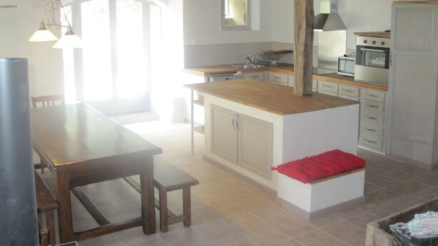 A kitchen with wooden beams, a dining table with benches, a small island with a red cushion, and a microwave. - House, charming cottage in the Cantal (Bassignac)