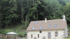A stone house with a sloped roof, multiple windows, and a chimney. - House, charming cottage in the Cantal (Bassignac)