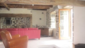 A room with a stone wall, a red sofa, a wooden chair, and a stove. - House, charming cottage in the Cantal (Bassignac)