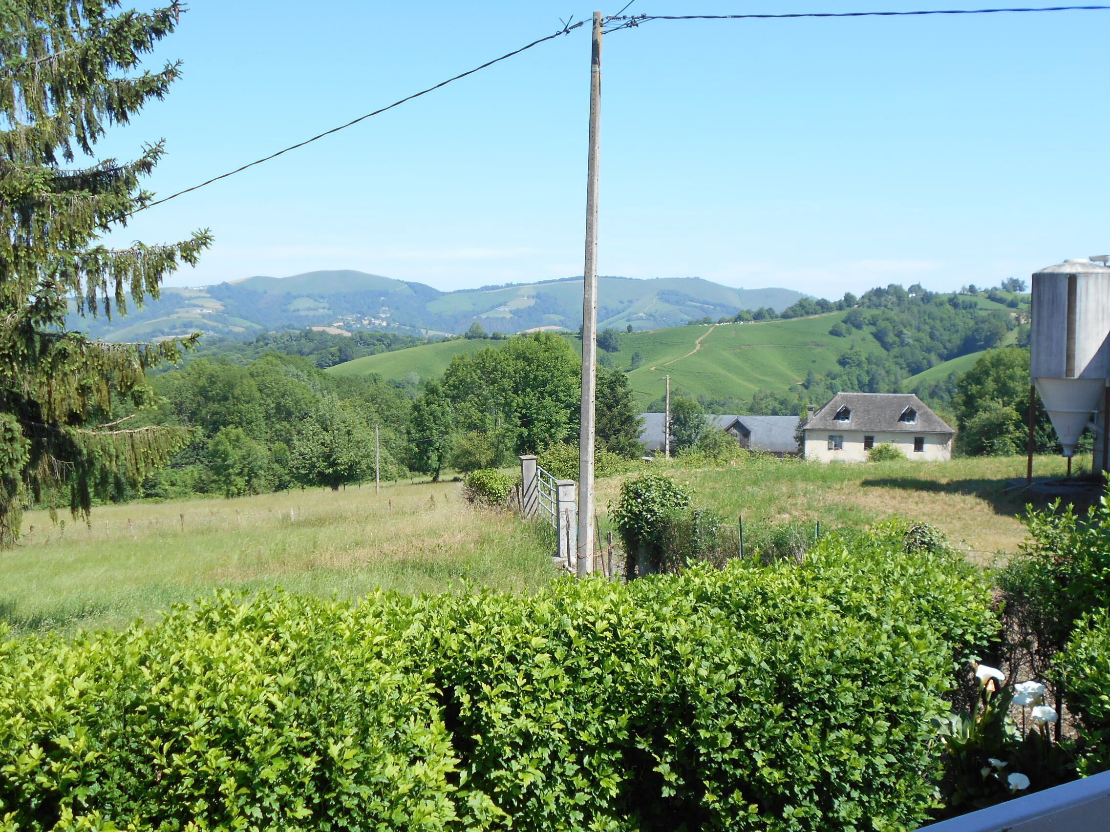 Un paysage rural avec des collines douces, une ferme et un poteau électrique.
