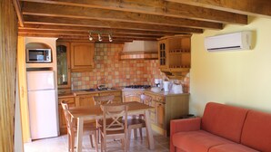 Una cocina compacta con armarios de madera, una mesa de comedor con sillas, un sofá rojo y un microondas.