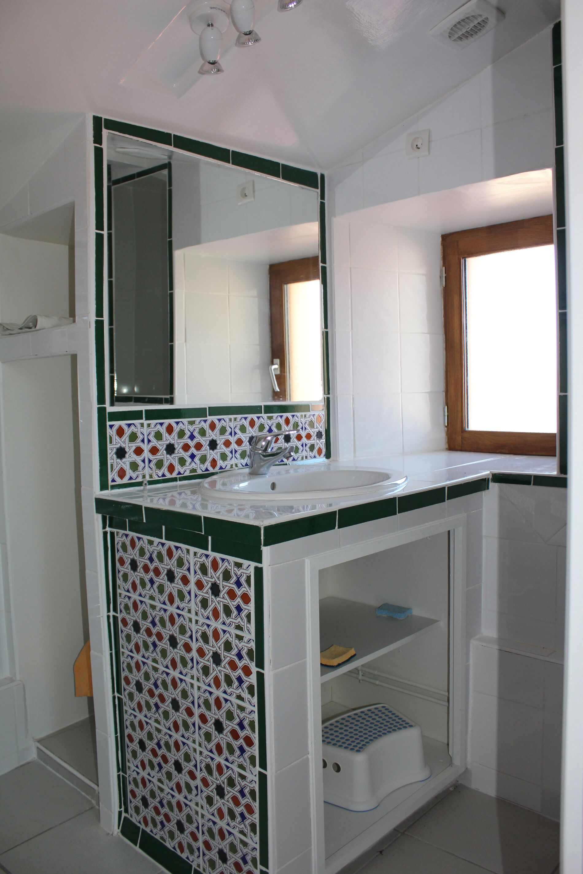 A bathroom with a white sink, green and white tiled backsplash, a mirror, and a window.