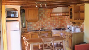 Una cocina compacta con armarios de madera, una mesa de comedor con sillas, un refrigerador y un microondas.