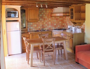 Une cuisine de taille réduite, avec des meubles de rangement en bois, une table à manger avec des chaises, un réfrigérateur et un four à micro-ondes.