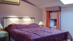 Un dormitorio con cama, mesitas de noche, un velador y una ventana con cortinas, además de un tragaluz.