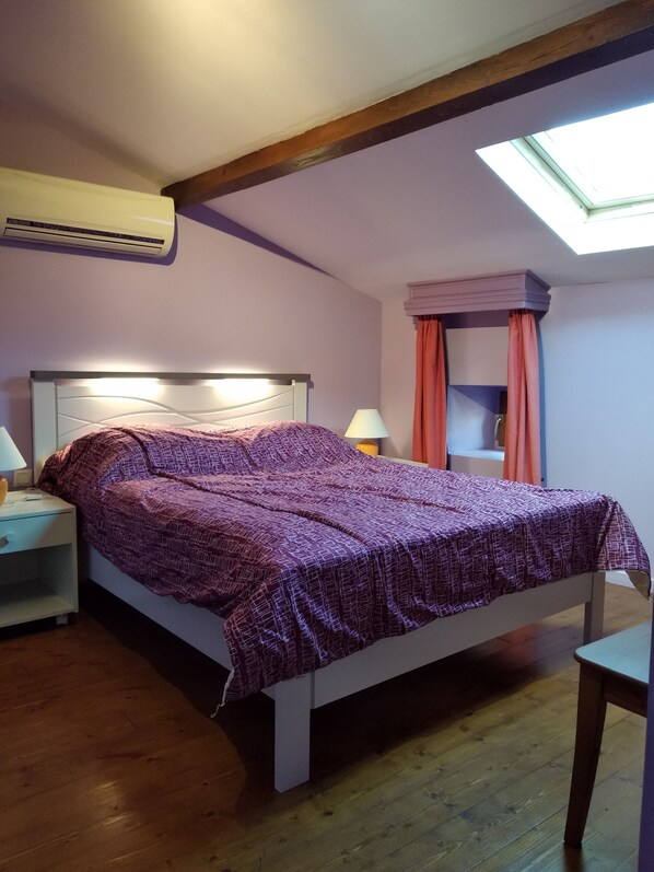 Ein Schlafzimmer mit einem Bett, Nachttischen, einem Fenster mit Vorhängen und einem Oberlicht.