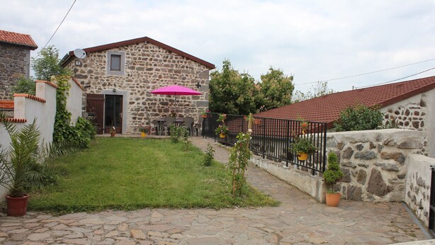 Una casa de piedra con tejado de tejas, un patio empedrado y un pequeño jardín con plantas en macetas.