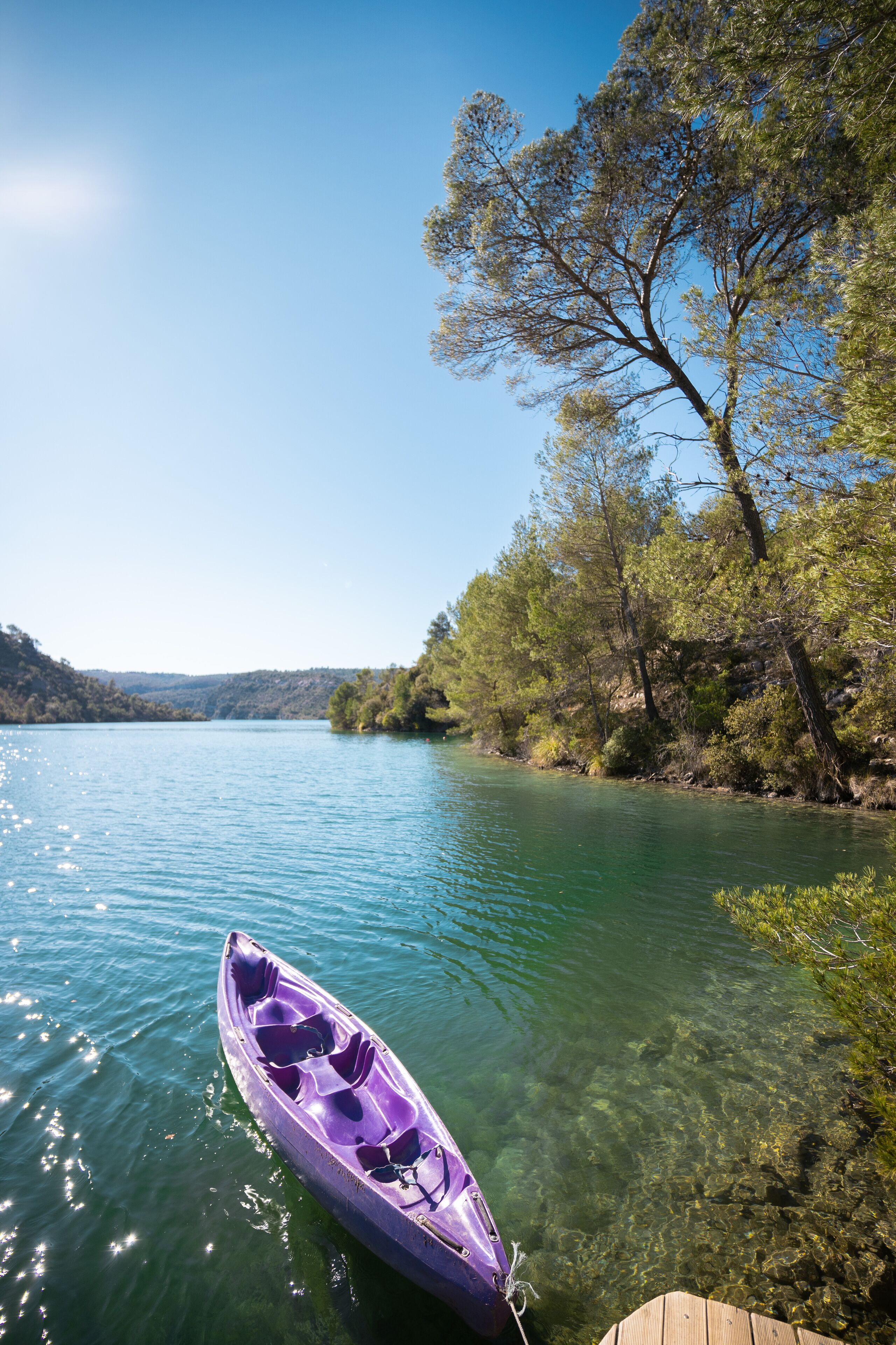 Un kayak amarrado a un muelle frente a un lago tranquilo bordeado de árboles.