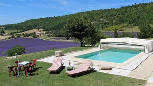 A swimming pool with lounge chairs and a table, surrounded by a grassy area and a view of a lake and hills. -  Between Ventoux and Luberon *** (Aurel)