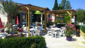 An outdoor patio with tables and chairs, a wooden pergola, and potted plants. - Camping Le Faillal - Cabanes et chalets (Montpezat-de-Quercy)