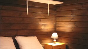 A wooden cabin bedroom with a bed, white pillows, and a bedside lamp. - Camping Le Faillal - Cabanes et chalets (Montpezat-de-Quercy)