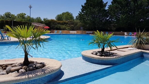 A swimming pool with clear blue water, surrounded by palm trees and rocks. - Camping Le Faillal - Cabanes et chalets (Montpezat-de-Quercy)