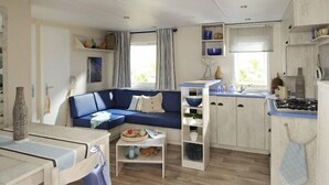 A compact living space with a sofa, dining table, kitchen area, and built-in shelves. - Camping Le Faillal - Cabanes et chalets (Montpezat-de-Quercy)