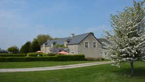A stone house with a well-maintained lawn and a tree with white blossoms. - House 20 mn from the beaches, 7 people, neat decoration, fully equipped (Crouay)