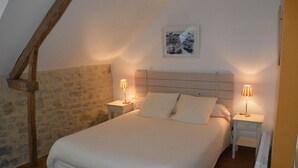A bedroom with a large bed, two bedside tables with lamps, a wooden ceiling beam, and a stone wall. - House 20 mn from the beaches, 7 people, neat decoration, fully equipped (Crouay)