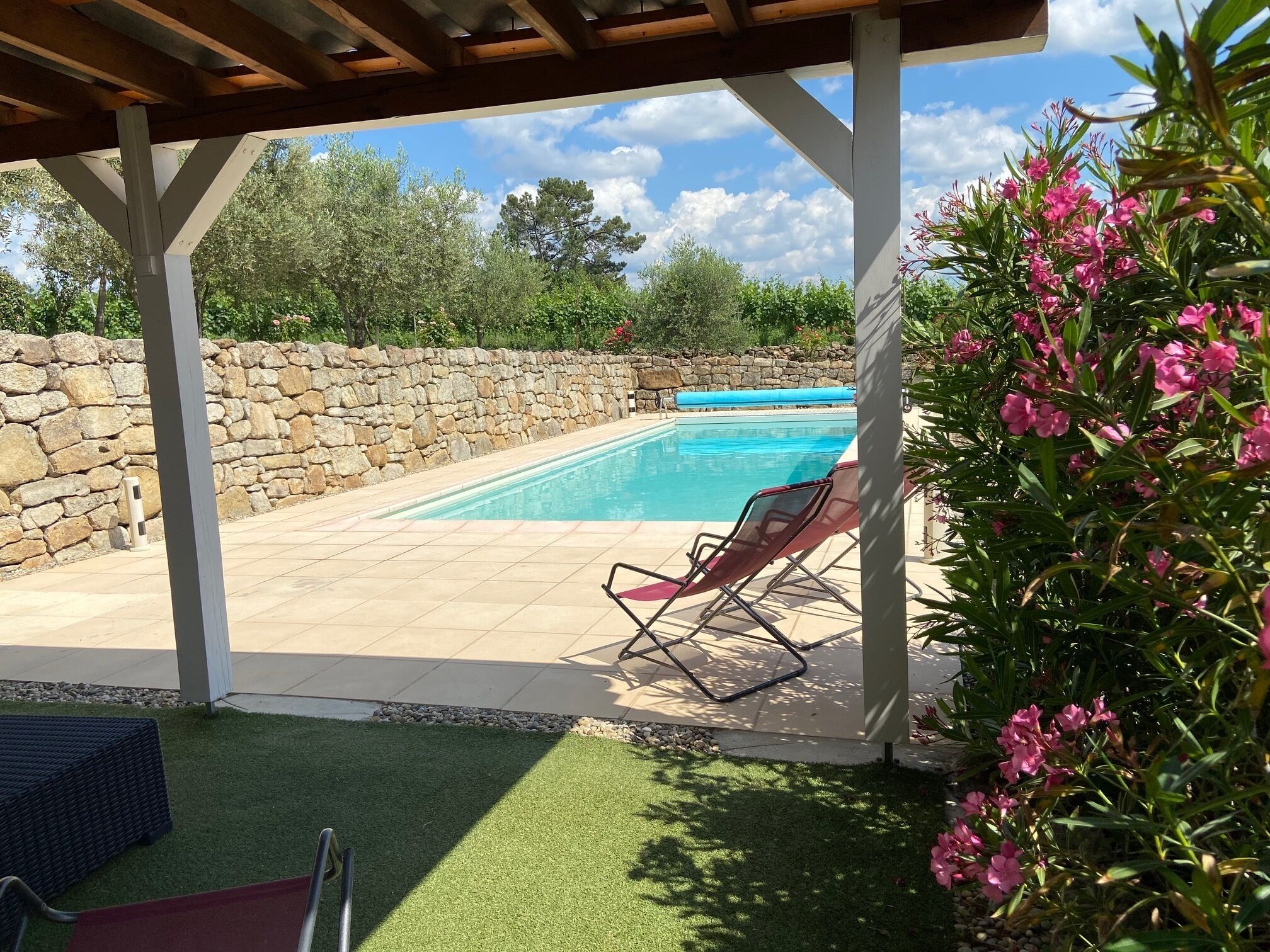 A covered outdoor area with a swimming pool, stone wall, and artificial grass.